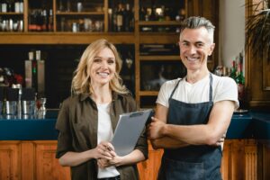 Small business owner with female auditor standing at bar restaurant cafe counter checking quality